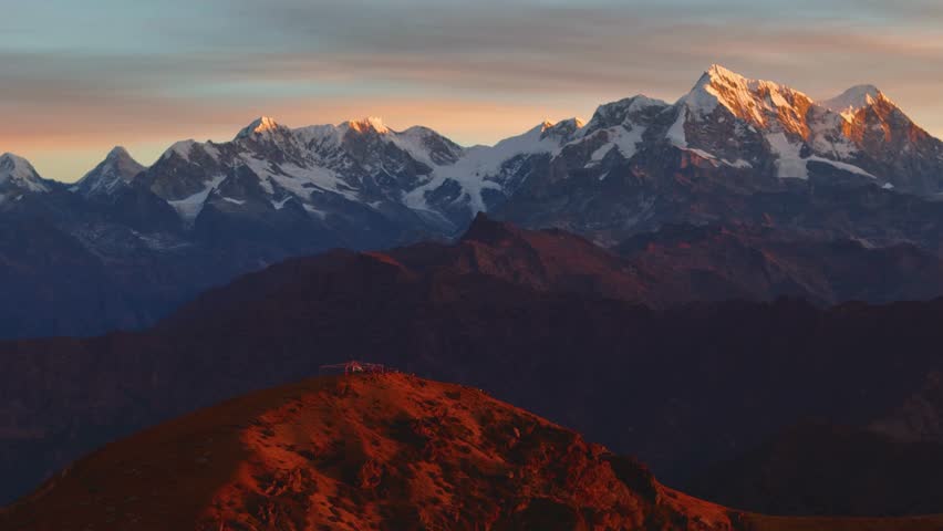This video captures the breathtaking beauty of a mountain range at sunset. The snow-capped peaks glisten in the fading light, while the foreground is ablaze with vibrant autumn foliage. The serene landscape stretches as far as the eye can see, inviting the viewer to immerse themselves in the natural splendor of this majestic scene. The video is a perfect representation of the awe-inspiring grandeur of nature, making it ideal for travel and adventure enthusiasts.
