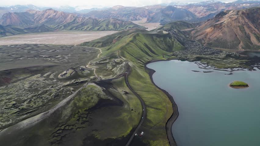 Aerial panoramic view of the colorful rhyolite mountains, volcanic landscape and lake in Landmannalaugar, Iceland. Dramatic highland scenery with green hills, lava fields and winding road in the Icelandic Highlands, popular destination for hiking and adventure travel.