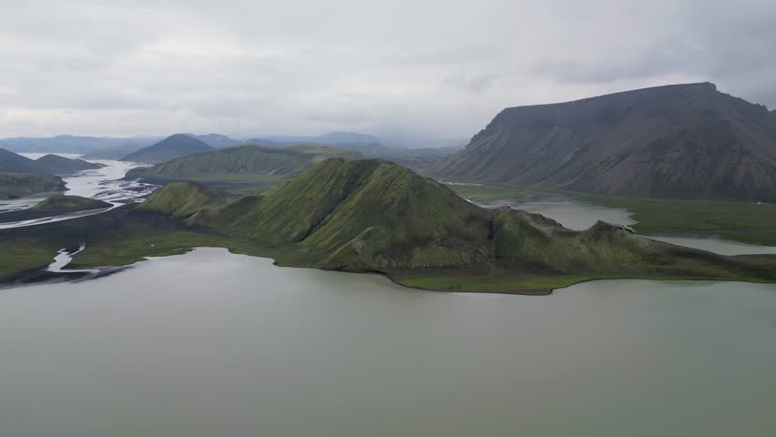 Aerial panoramic view of the colorful rhyolite mountains, volcanic landscape and lake in Landmannalaugar, Iceland. Dramatic highland scenery with green hills, lava fields and winding road in the Icelandic Highlands, popular destination for hiking and adventure travel.