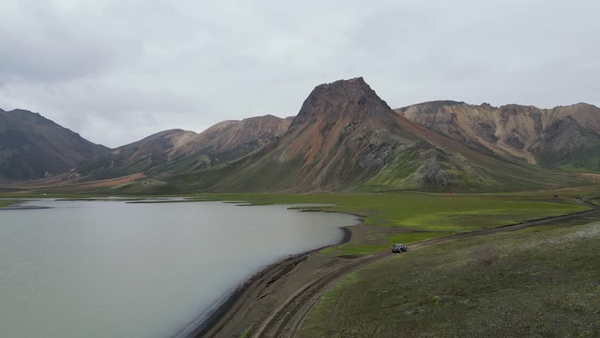Aerial panoramic view of the colorful rhyolite mountains, volcanic landscape and lake in Landmannalaugar, Iceland. Dramatic highland scenery with green hills, lava fields and winding road in the Icelandic Highlands, popular destination for hiking and adventure travel.
