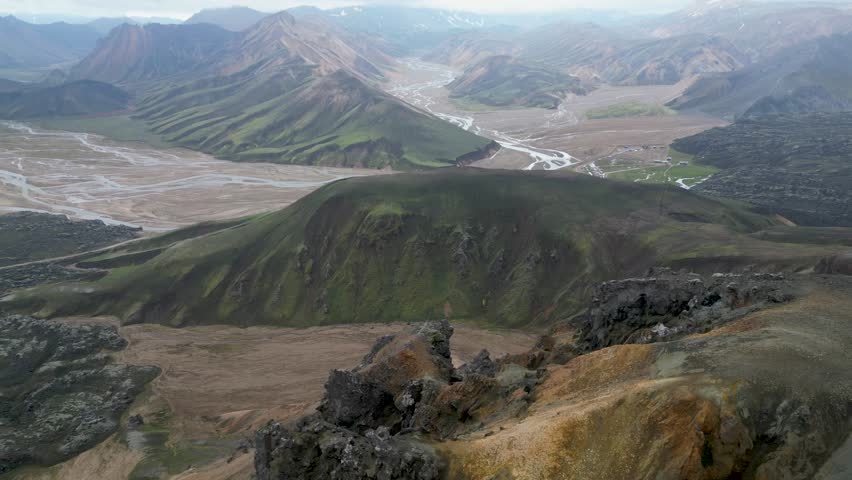 Aerial panoramic view of the colorful rhyolite mountains, volcanic landscape and lake in Landmannalaugar, Iceland. Dramatic highland scenery with green hills, lava fields and winding road in the Icelandic Highlands, popular destination for hiking and adventure travel.
