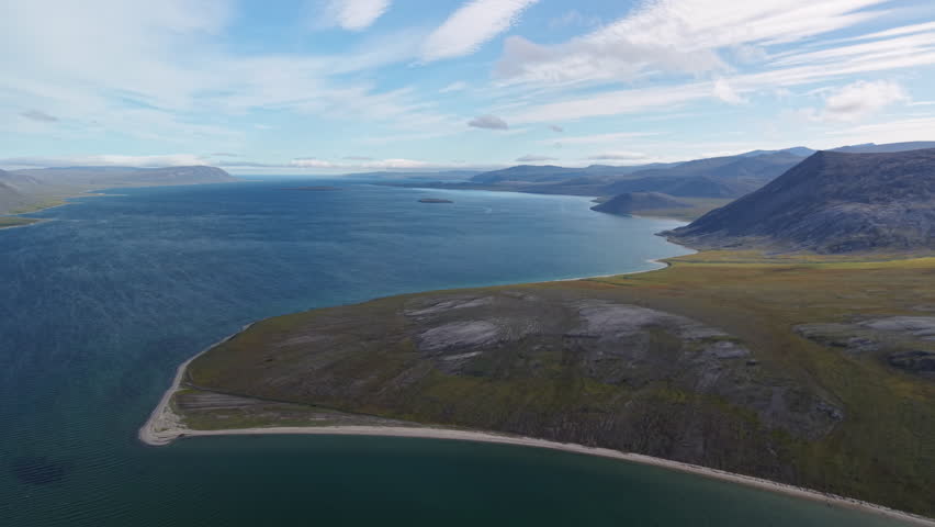 Aerial view across Lavrentiya Bay toward low island and a long sandy spit with blue horizon, clear sea and raw tundra land in bright weather ideal for tourism brochure, expedition visual and geography