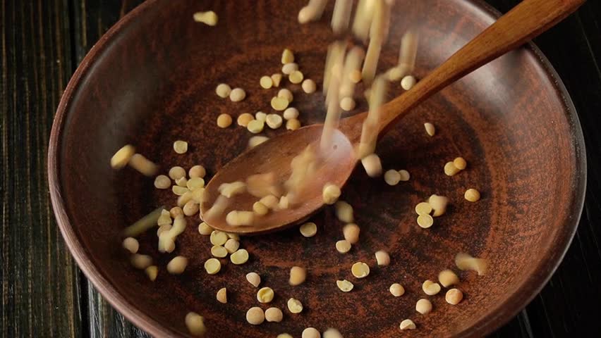 Peas are poured into an old-fashioned bowl with a wooden spoon before making porridge. Preparing legumes for cooking dinner.