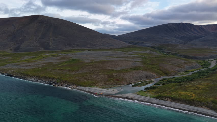 Overcast summer morning near Provideniya and Gilmimyul Bay, Chukotka, Russia. Gentle side drift tracks the coast and braided river. Cold sea and tundra valley fill the frame for adventure
