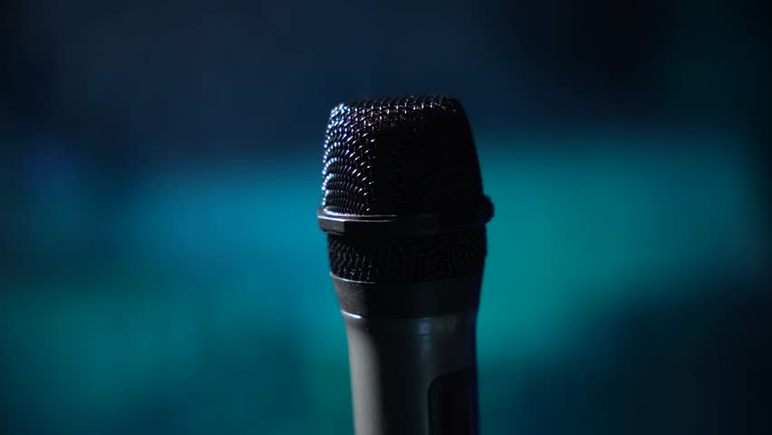 Professional handheld microphone in dramatic blue stage lighting. Close-up view with dark background ideal for music, podcast or performance concepts.