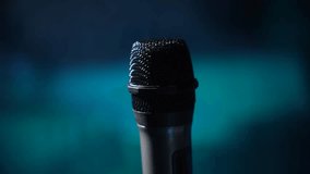 Professional handheld microphone in dramatic blue stage lighting. Close-up view with dark background ideal for music, podcast or performance concepts. - Powered by Shutterstock - Get 15% off with code: PIKWIZARD15