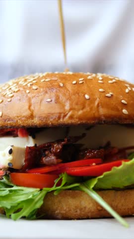 Delicious gourmet burger with fresh ingredients such as arugula, sun dried tomatoes, and mozzarella on a plate while a chef