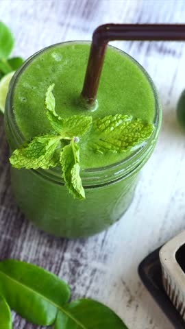 Refreshing green vegetable smoothie in a glass jar garnished with a fresh mint sprig and served with lime on a rustic wooden table, representing a healthy detox diet and vegan lifestyle