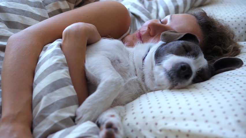 Adorable puppy and its owner sleeping together peacefully in bed, creating a heartwarming scene of love and companionship between a human and her pet during a quiet morning rest