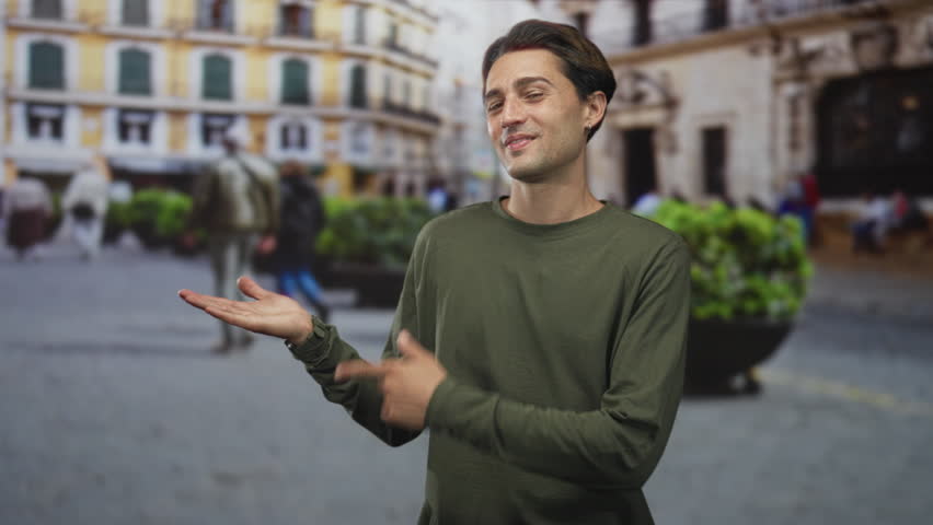 Man pointing finger to open palm while presenting with hand on street, casual smile and earring visible; confidence approachable charm.