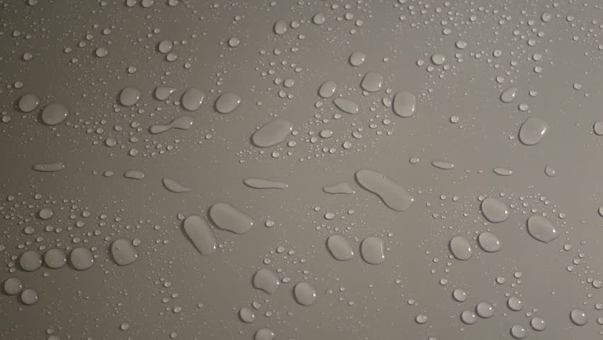 Numerous drops of water are visible on the gray surface after the jet hits. The surface is slightly shaken, which causes the droplets to connect and move faster. Small droplets merge into larger ones and slide rapidly through the material, shifting to the side.

The smooth surface is covered with a multitude of water droplets of various sizes. After the water flow stops, the droplets remain on the material and gradually change shape, connecting with each other. Small fluctuations in the surface cause the accelerated movement of water