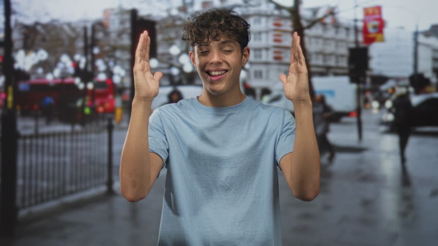 Teenage boy smiling with thumbs up gesture on a busy city street near railing and vans; youthful joy.