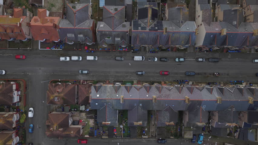 Top down aerial drone view of a UK residential street with terraced houses, rooftops and parked cars. Overhead urban neighbourhood layout showing housing and road infrastructure in a British town, property and real estate concept.