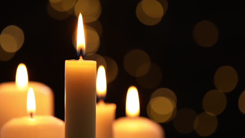 Burning candles against black background with blurred lights, closeup
