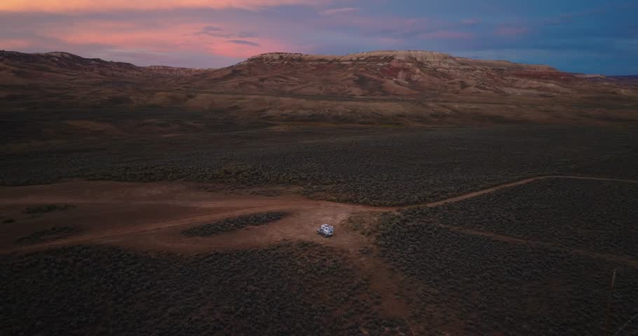 Aerial view of dirt road crossing sagebrush desert with layered buttes at sunset in Wyoming