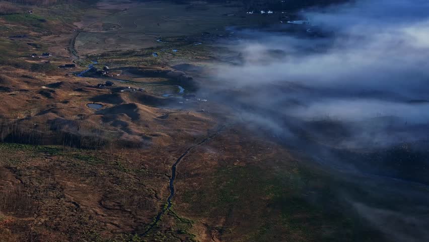Low clouds sliding across forested lakeshore with mountain ridge beyond water