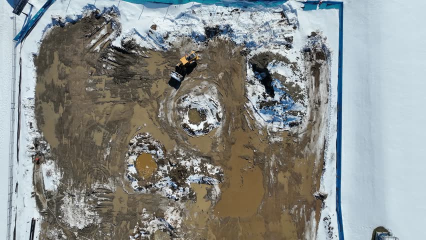 Aerial view of a snowy construction site with an excavator working