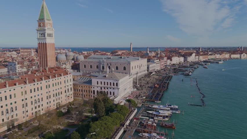 Horizontal drone shot descending over Saint Marks Square in Venice with view of the Campanile and nearby canal surrounded by historic architecture.