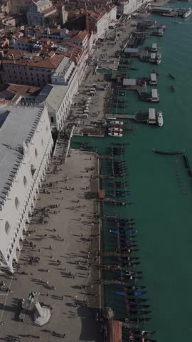 Vertical drone shot descending along the canal in Venice showing the Doge Palace and the canal with surrounding historic buildings.