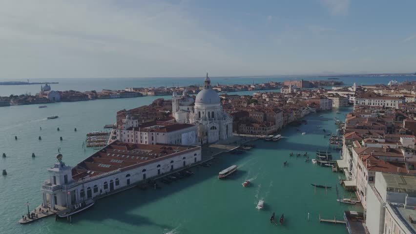 Horizontal drone shot rising from Basilica Santa Maria della Salute in Venice showing the canal, boats, and the cityscape in the background.