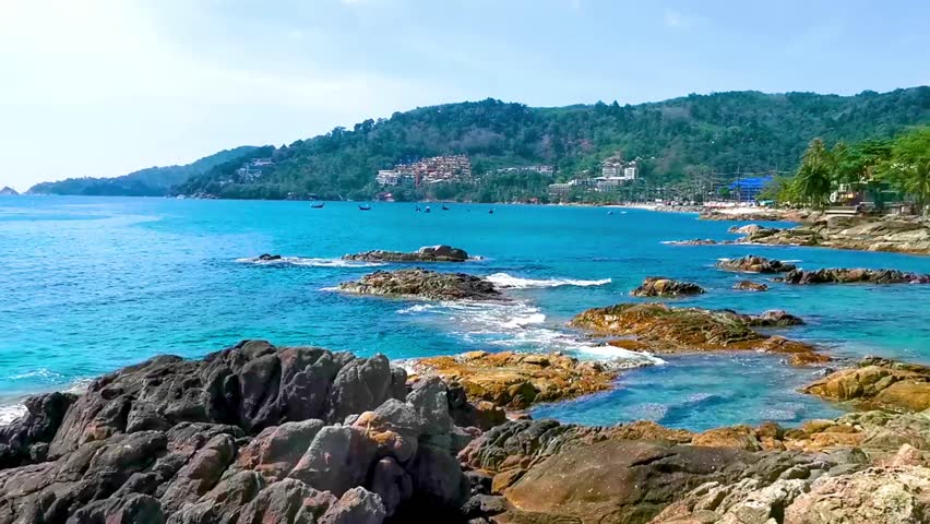 Tropical Kalim Beach rocky seascape shore coast with turquoise blue green clear water waves sand boulders stones and rocks in Patong Beach Kathu District Phuket Island Province Southern Thailand.