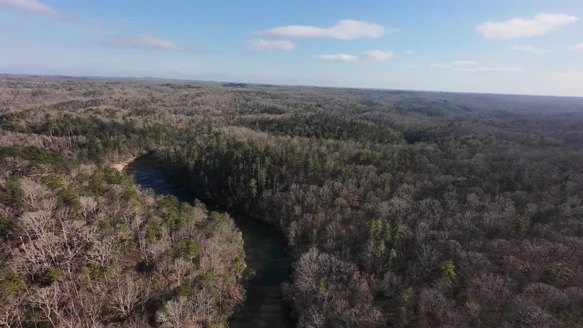 Cinematic aerial drone footage of the Upper Chattahoochee River winding through the forested landscape of North Georgia. Captured in natural light, the river curves between hardwood trees and rolling hills, creating a peaceful southern wilderness scene. Ideal for travel, tourism, environmental conservation, and nature background content.