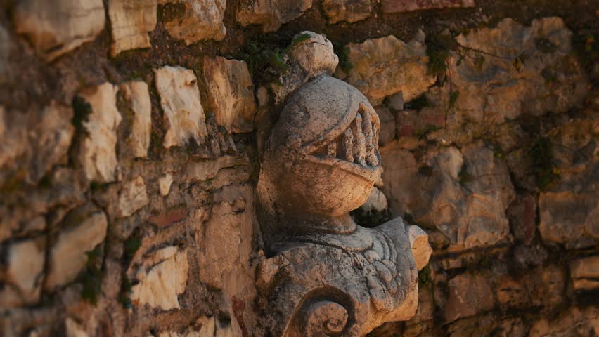 Weathered stone carving of medieval knight with armored helmet and visor in wall at Castello di Brescia, Italy