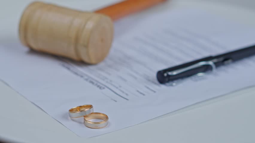 Two gold wedding rings on divorce decree papers with a wooden judge gavel and pen