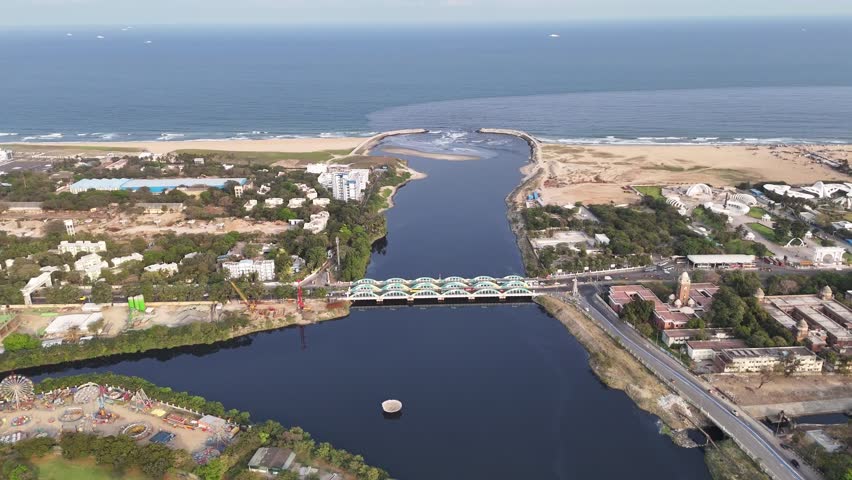 Aerial view of the Cooum River meeting the Bay of Bengal at Marina Beach, Chennai, framed by curved breakwaters and sandy shores. Urban buildings and greenery line the riverbanks before it opens into