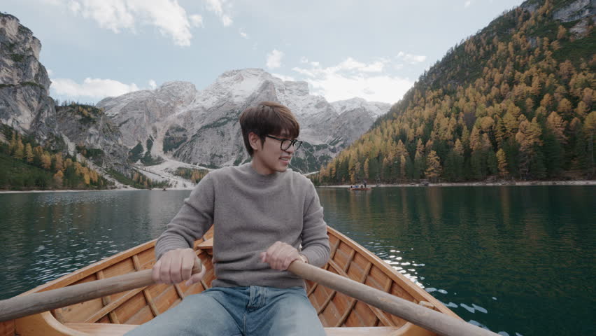 A man sitting in a traditional wooden boat on the turquoise waters of Lago di Braies in the Dolomites, Italy. Scenic alpine lake surrounded by mountains during summer vacation.	