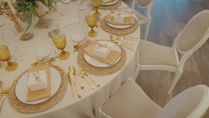Overhead view of ivory wedding table with gold cutlery amber goblets woven chargers and ribbon favor boxes