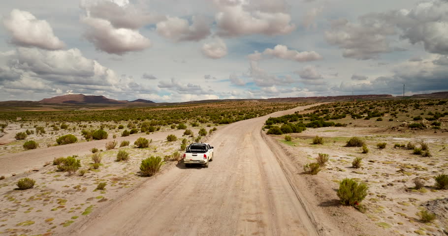 Aerial tracking follows pickup truck driving dirt road in Sioli Desert Bolivia under cloudy sky, medium