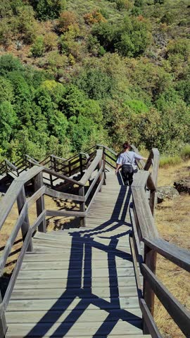 Young woman walking down a long wooden staircase on a sunny day in a rural landscape