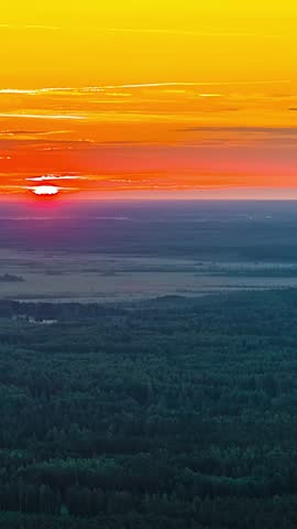 Sunrises over forest and open forested fields with vivid orange sky, vertical timelapse backdrop