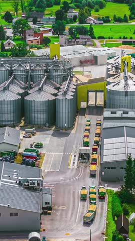 Grain silos and processing facility with trucks offloading and exiting through weighing station, vertical