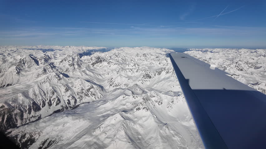 Breathtaking aerial view from a small aircraft flying over the snow-covered Swiss Alps. The airplane wing in the foreground frames an expansive panorama of rugged alpine peaks, deep mountain valleys