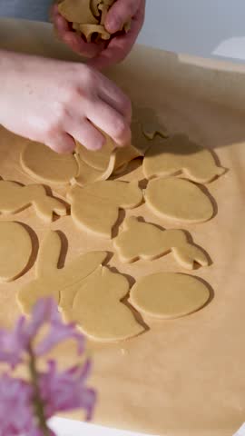 Hands work with dough to create Easter cookies in a kitchen. Shapes are cut from the dough, focusing on different designs for the holiday celebration.
