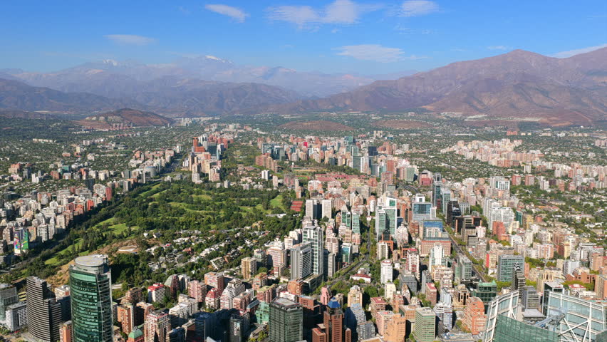 Costanera Center office building and Santiago cityscape, Chile. Parque Araucano, Andes mountain range, and El Plomo glacier in the background in sunny summer afternoon sky. Wide aerial pull back in 4K
