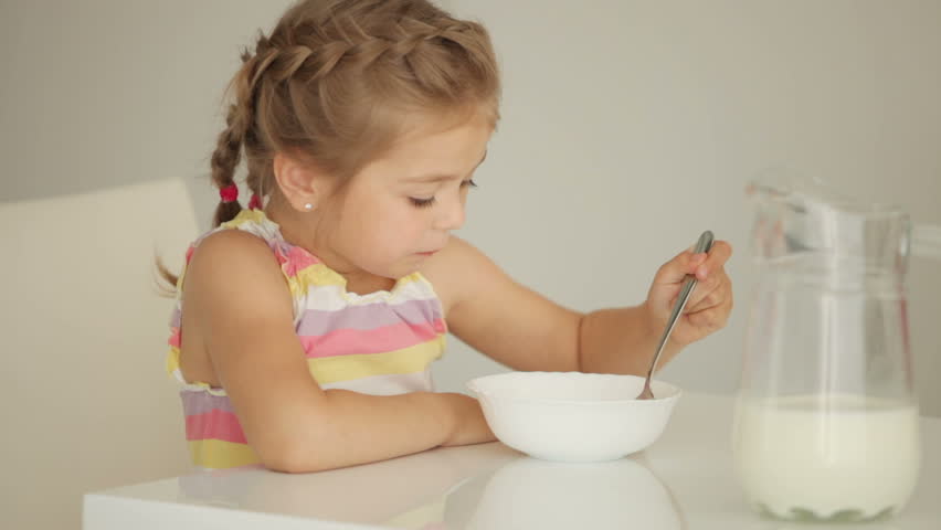 Little girl eating cereal with milk and smiling

