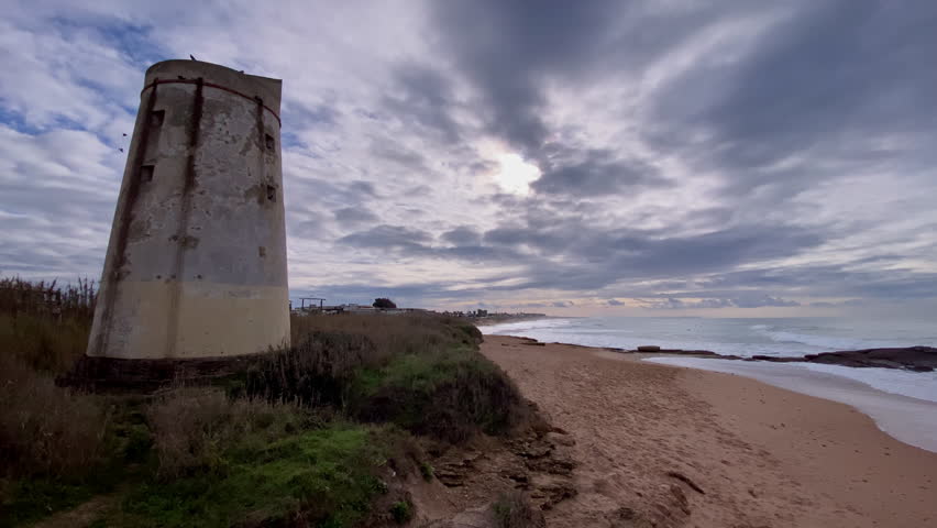 Historic tower standing on a coastal cliff overlooking a sandy beach and the Atlantic Ocean under a cloudy sky