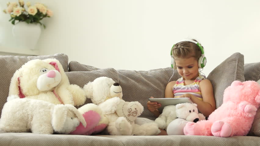 Little girl sitting on the couch with a tablet pc and listen to music
