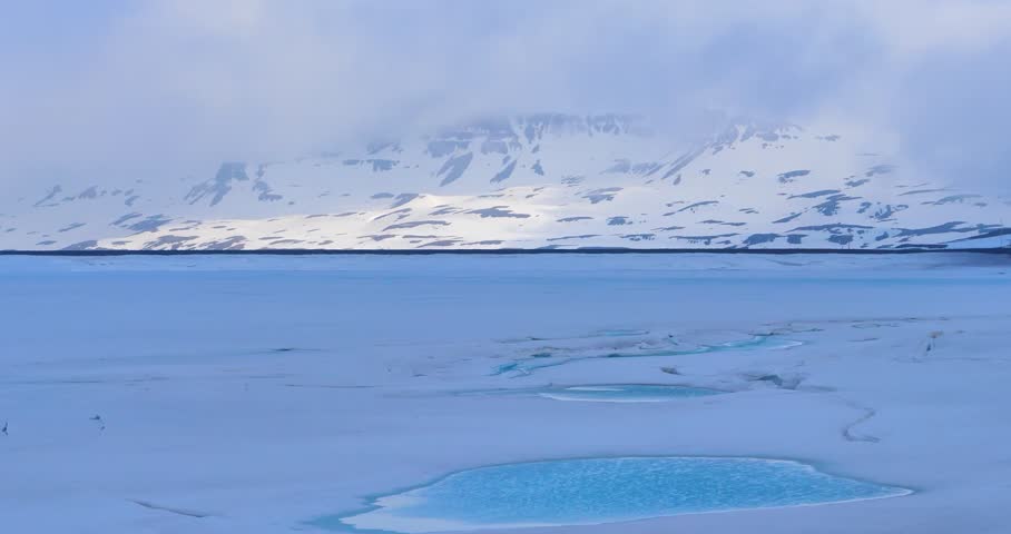 This video captures an Arctic environment featuring a frozen water surface and snow-covered terrain. The visual documents ice formations and distant mountain peaks under a clear sky. The composition illustrates high-latitude geography and cryospheric features, documenting polar topography and winter conditions in a high-resolution 4K format for environmental and editorial media.