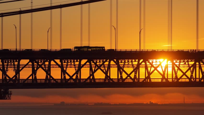 Aerial view of sunset in Lisbon with an iron suspension bridge and heavy urban traffic, urban scene, drone shot of transportation on the road with a setting sun