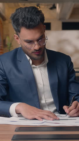Arabian business man writing in office businessman happy smiling at camera finish write notes in documents stats diagram data review paperwork Indian guy male worker signing job contract report joyful
