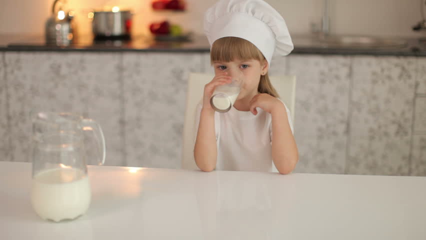 Little girl sitting in the kitchen and drinking milk
