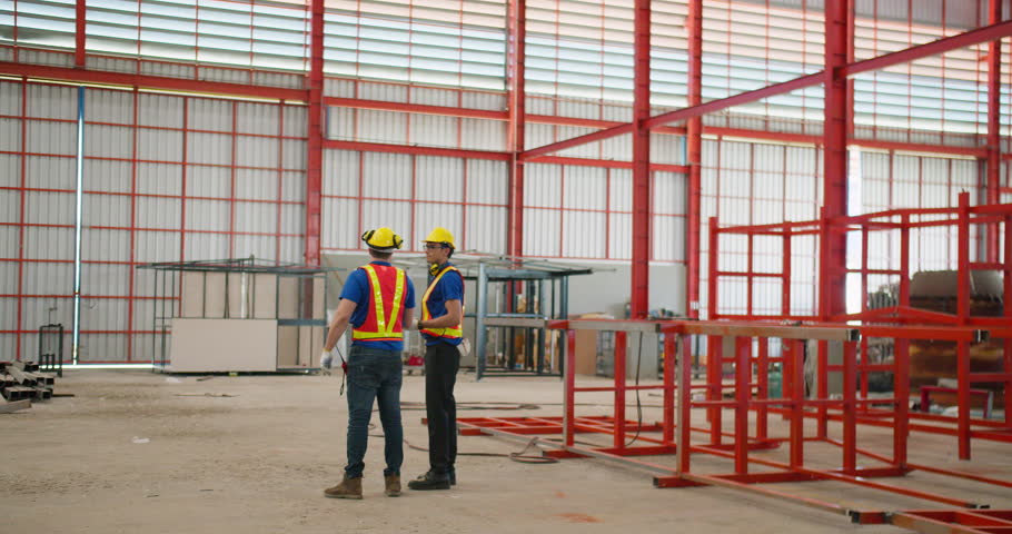 Two professional engineers are collaborating on a new construction project in a large factory, focusing on industrial safety, quality control, and project management.