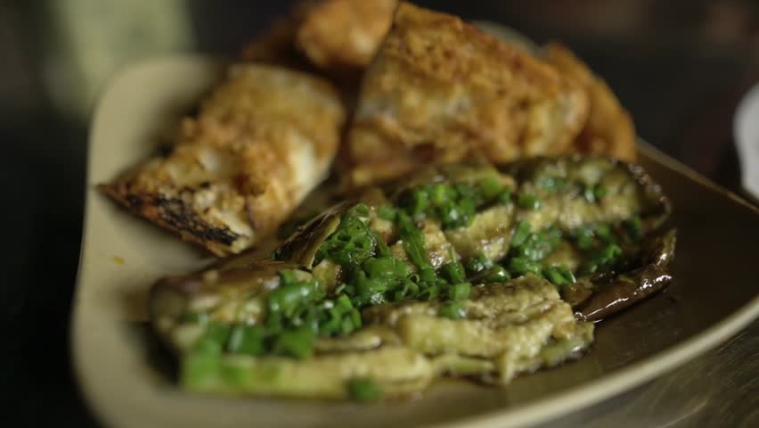Grilled Eggplant Topped With Scallions And Eggrolls On Plate, Vendor Plating In Warm Lowlight Vietnamese Street Market, Smoky Char, Crispy Texture, Closeup Food Composition
