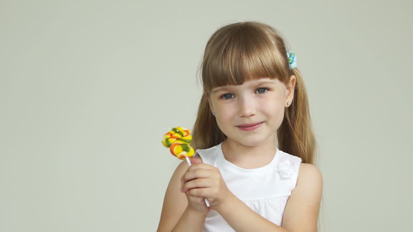 Little girl stands with a lollipop and smiling
