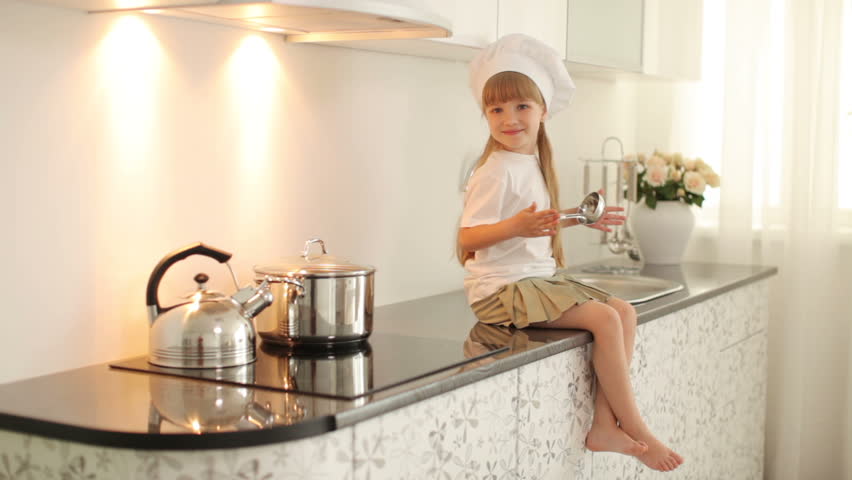 Little girl sitting in the kitchen with a ladle in hand
