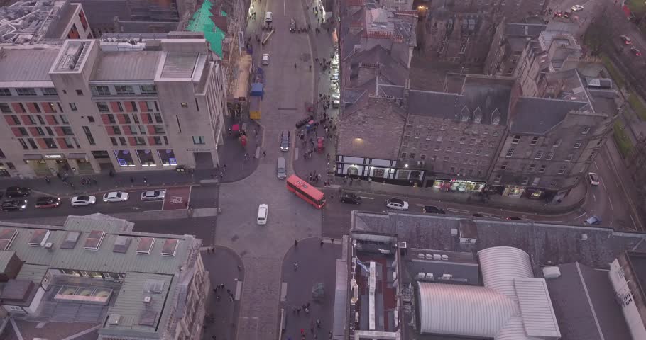 Aerial view of Edinburgh in Scotland featuring the historic Edinburgh Castle dominating the skyline above the Old Town. The elevated perspective reveals a dense urban fabric composed of traditional stone buildings, narrow streets and layered rooftops extending across the city. Soft natural light enhances architectural details while surrounding hills create depth and contrast within the composition, highlighting the unique topography of the Scottish capital.

The castle stands prominently on volcanic rock, reinforcing its strategic importance and cultural significance throughout centuries of history. The scene captures the balance between heritage and urban life, with historic districts blending into more modern areas while maintaining a cohesive visual identity. Subtle atmospheric conditions add mood and realism, emphasizing textures across rooftops, facades and open spaces.

This footage represents one of the most iconic city views in the United Kingdom, widely recognized for its preserved architecture, historic landmarks and dramatic setting. Ideal for travel, tourism, cultural storytelling and editorial use, the image conveys a strong sense of place rooted in European history and landscape.
